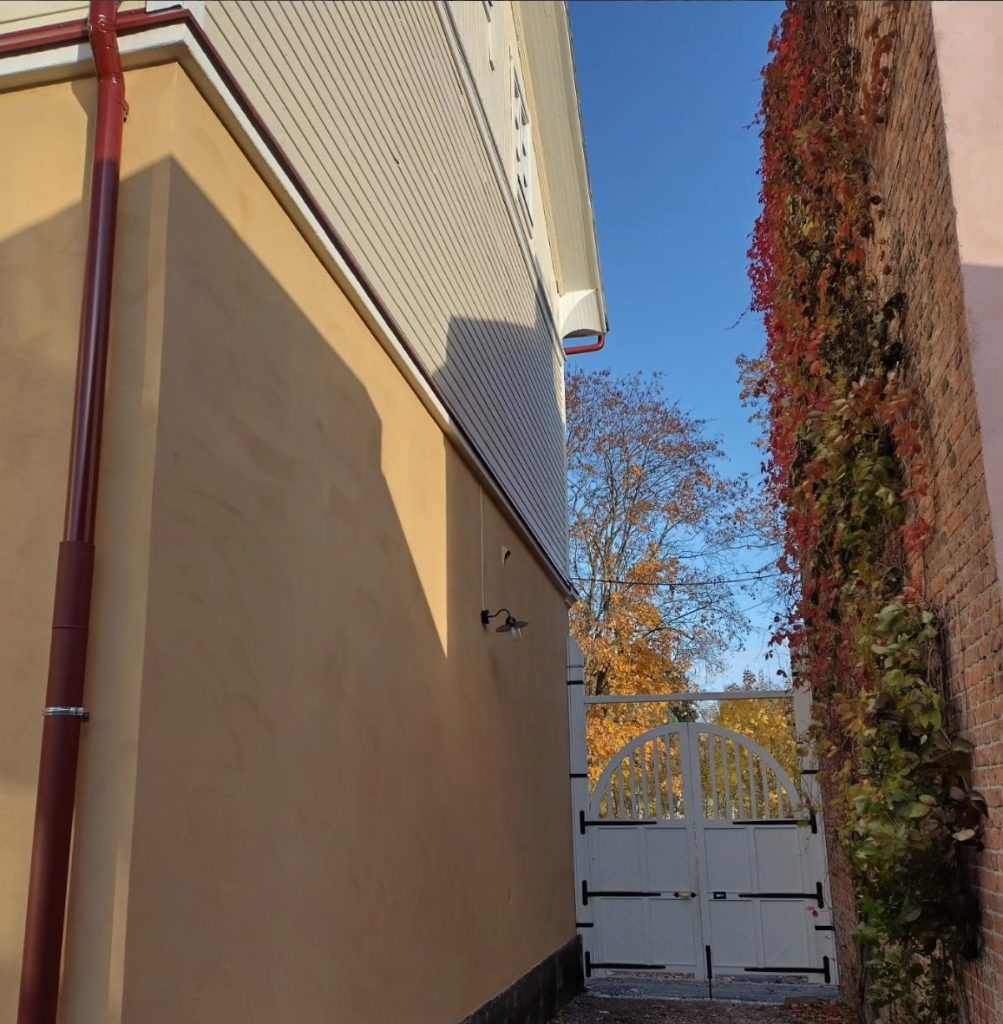 Kalkkimaalattu rappauspinta ja punainen syöksytorvi syysvalossa